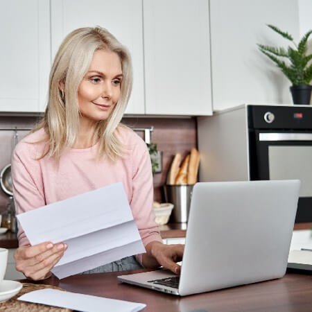 Woman holding letter while looking at laptop | The hidden charges eroding your pension